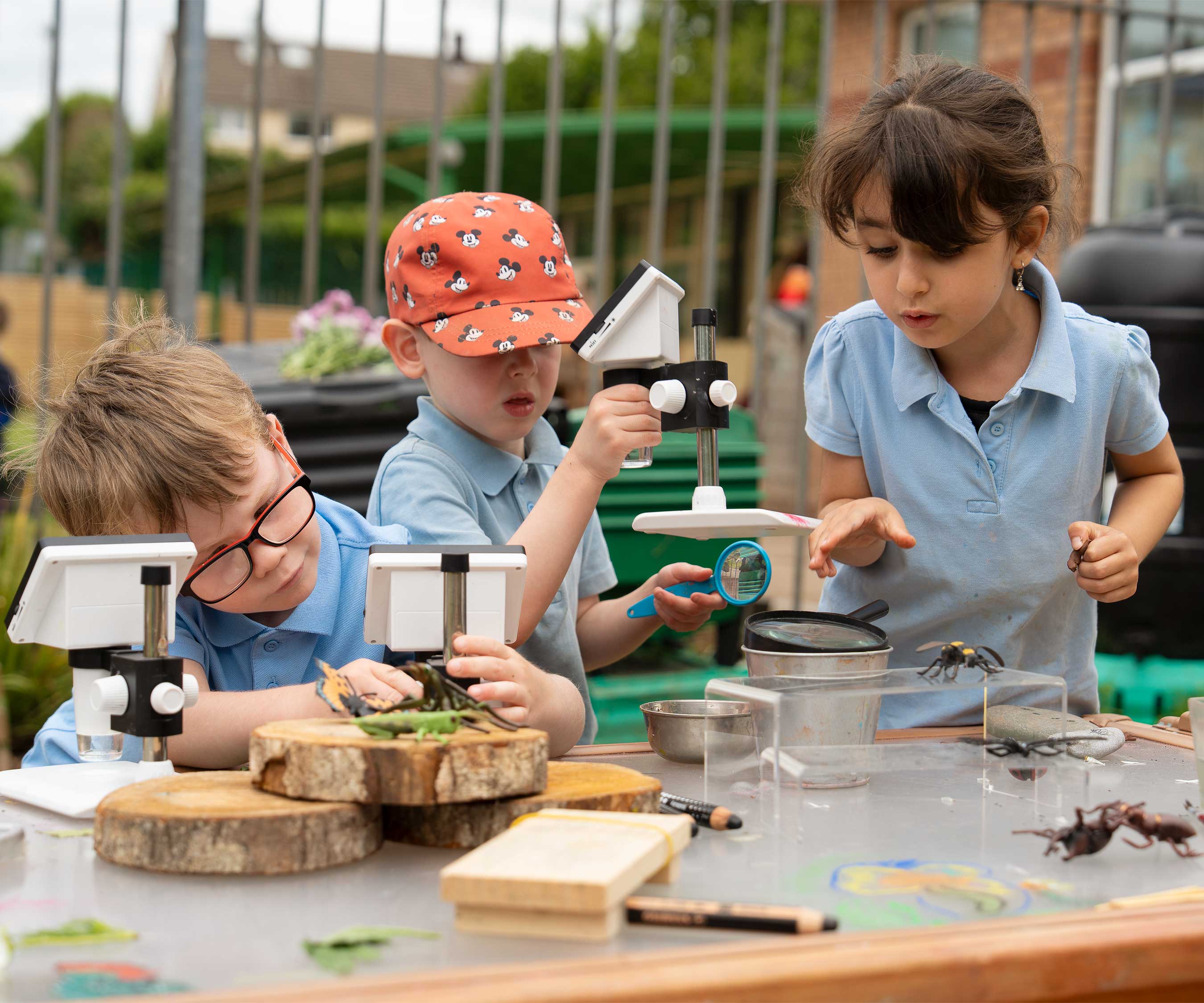 Grundschulkinder benutzen Mikroskope und wissenschaftliche Geräte an einem Kunsttisch im Freien.
