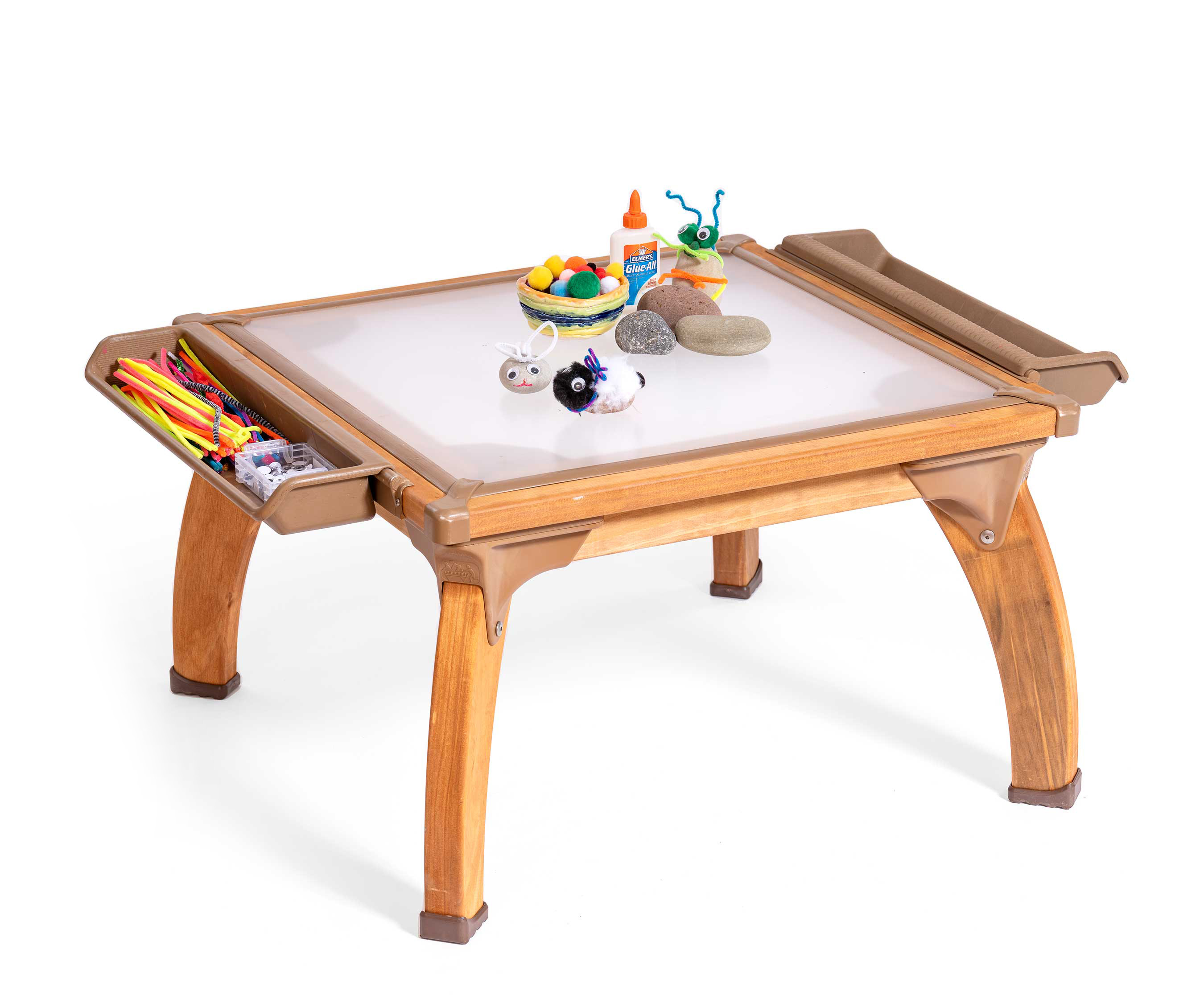 Ein Kunsttisch mit durchsichtiger Platte, auf dem Kieselsteine, Kleber und Farbe für ein Kunstprojekt bereitliegen.