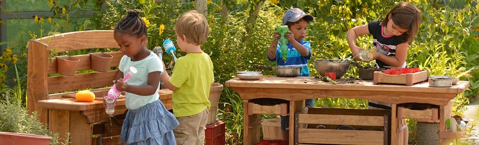 Four preschool age children are playing with a mud kitchen sink and counter