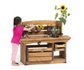 A girl is scooping a sunflower out of a container clipped onto the splashback of a mud kitchen sink