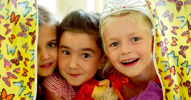 Drei Mädchen schauen durch einen Vorhang und lachen