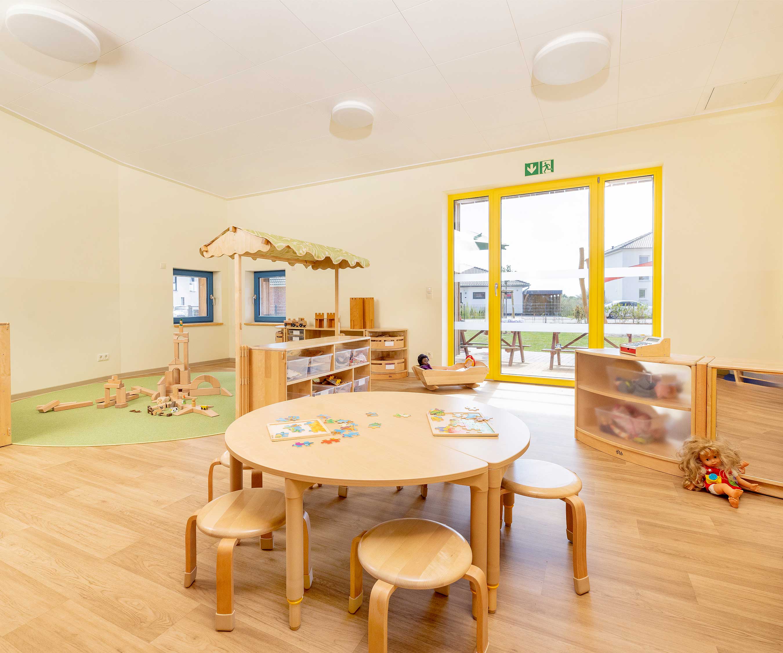 Einrichtung eines neuen Kindergartens mit Massivholzmöbeln, darunter Tische, Stühle, Regale und ein Puppenbett.