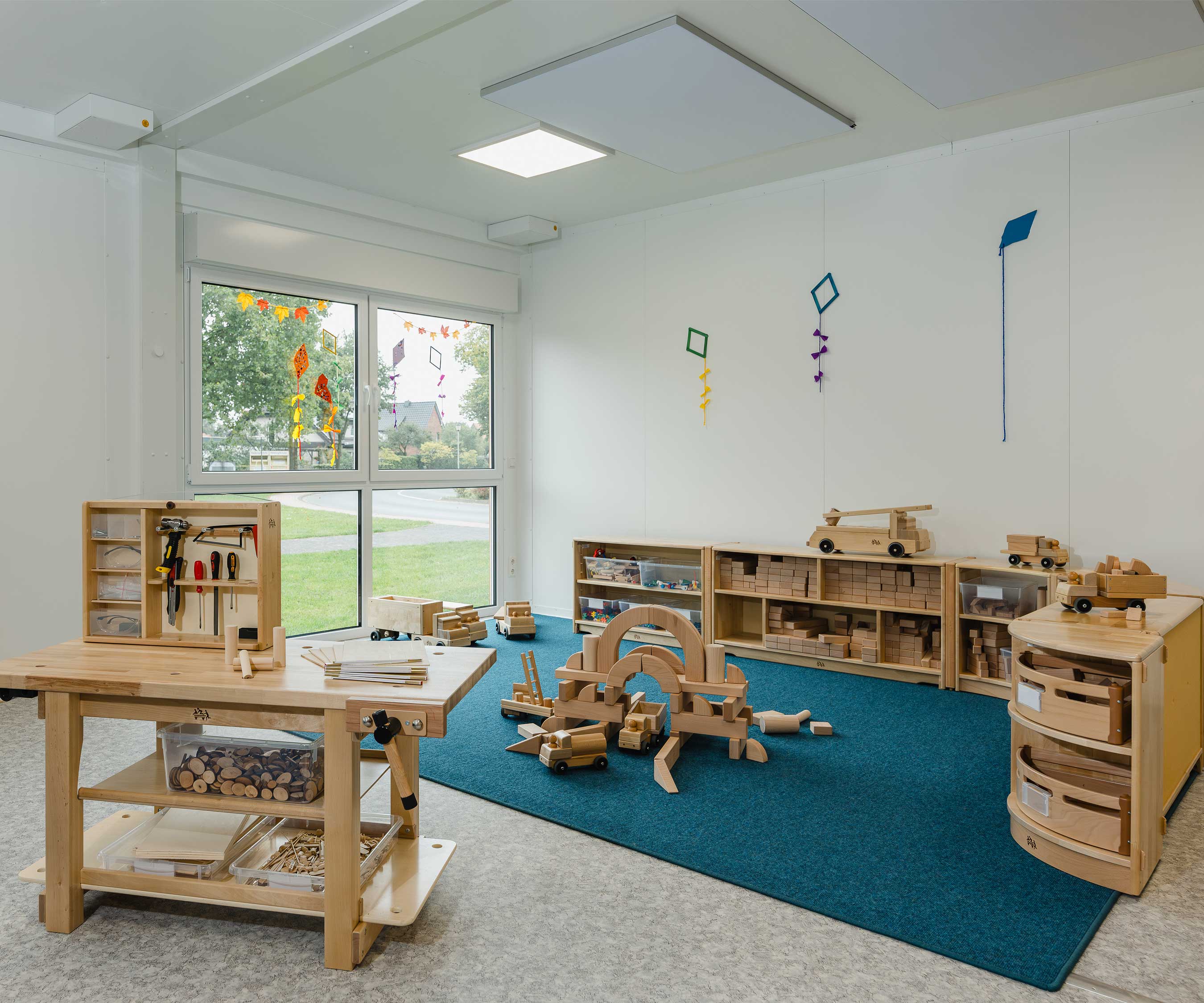 Ein Bausteinbereich, der auf einem rechteckigen blauen Teppich eingerichtet ist, mit einer Werkbank im Vordergrund.