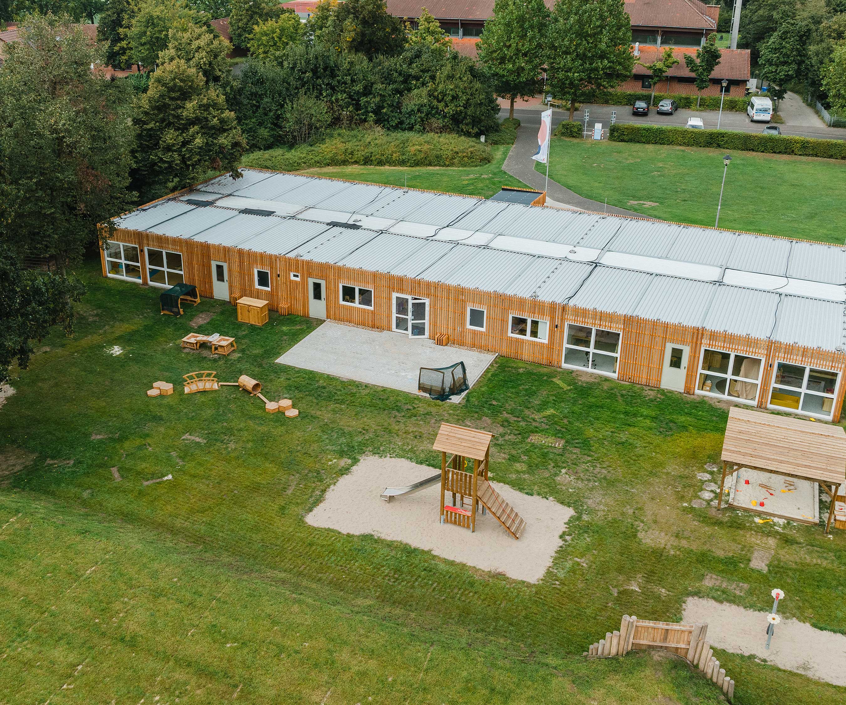 Ein Blick auf ein Kita-Geb&amp;#228;ude, das von einem Au&amp;#223;enbereich umgeben ist, der Outlast Podeste, eine Outlast Br&amp;#252;cke und einen Outlast Tunnel umfasst.