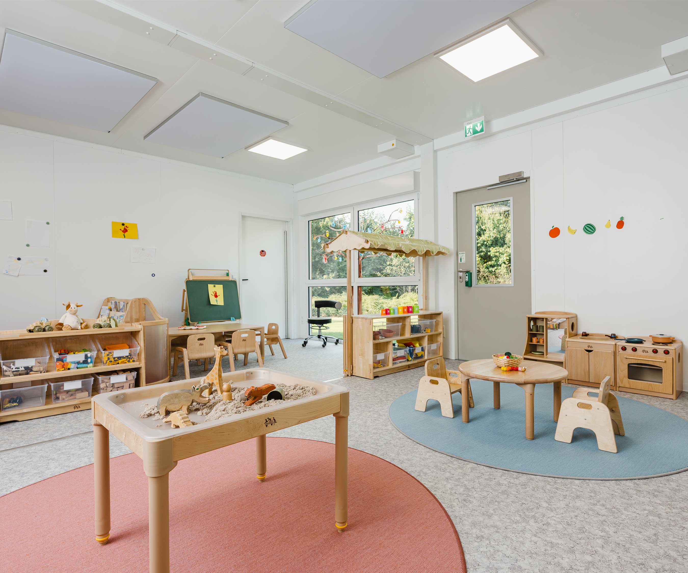 Ein Sand- und Wassertisch zum Spielen auf einem roten Teppich und eine Rollenspielk&amp;#252;che auf einem blauen Teppich.